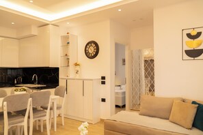 Ein modernes Wohnzimmer mit einer Couch, Sesseln, einem Essbereich mit Tisch und einer Küche mit schwarzer Arbeitsplatte.