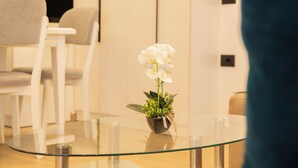 A glass table with a potted orchid, white chairs, and a white cabinet in the background. - Villa Rafail (Ksamil)