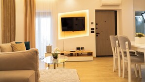 A modern living room with a flat-screen TV mounted on the wall, a glass coffee table, a sofa, and a dining area with chairs. - Villa Rafail (Ksamil)