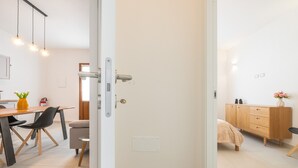 An open door leading to a room with a bed, a wooden dresser, and a dining area with chairs and a table. - 'Luxi Teulada' Apartment with Wi-Fi and Air Conditioning (Teulada)
