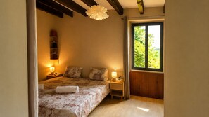 Ein Schlafzimmer mit Bett, Nachttischlampen, einem Fenster mit Blick und einem Holzbalken an der Decke.
