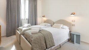 Quarto de hotel com duas camas, uma mesinha, uma luminária e uma janela com cortinas.