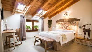 A bedroom with a stone fireplace, wooden ceiling beams, a bed, a bench, and a desk with a chair. - El Patio de la Morera I and II (El Rasillo de Cameros)