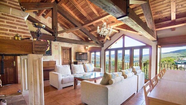 A spacious living area with a high ceiling, a fireplace, a sofa set, and a dining table. - El Patio de la Morera I and II (El Rasillo de Cameros)