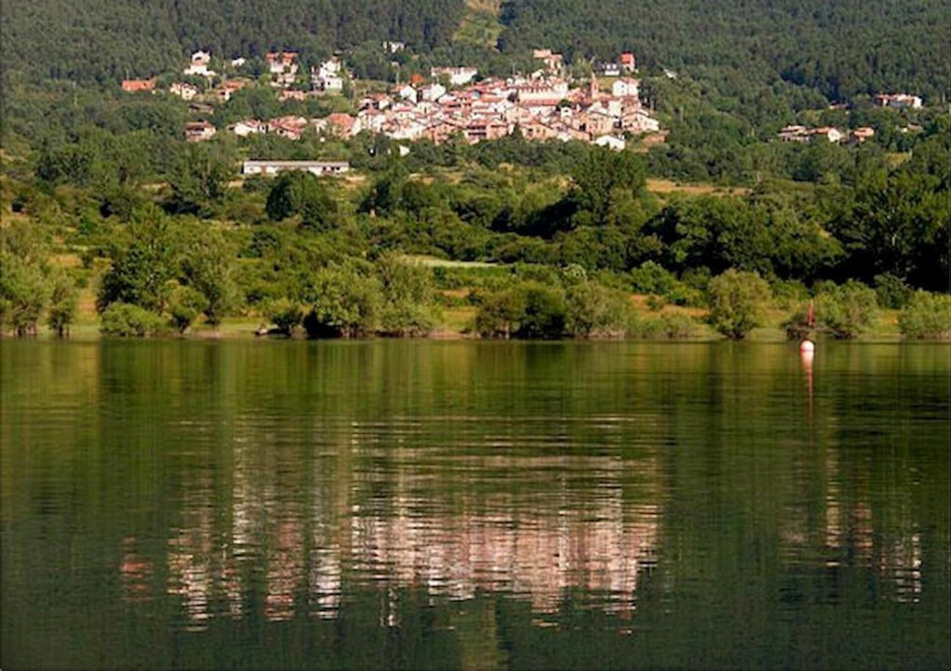 Un lago con un pueblo en la orilla opuesta, rodeado de vegetación.