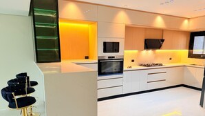 A modern kitchen with white cabinets, a built-in oven, and a TV. - 5 Rooms with private garden& Jacuzzi& Pool acc (New Administrative Capital)