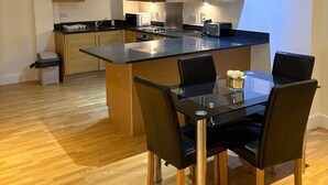 A modern kitchen with wooden cabinets, a central island, and a dining area with a glass table and chairs. - Central Luxurious Apartment London Bridge (London)