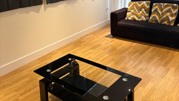 A living room with a black glass coffee table, a dark sofa with patterned cushions, and black curtains. - Central Luxurious Apartment London Bridge (London)
