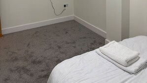 A bedroom with a flat-screen TV mounted on the wall, a power outlet, a carpeted floor, and a neatly made bed with a folded white towel. - Central Luxurious Apartment London Bridge (London)