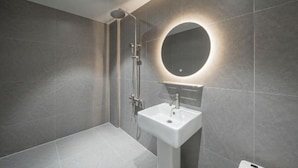 A modern bathroom with a shower, a sink, and a round mirror with a light. - DEUMEU HOTEL (Changwon)
