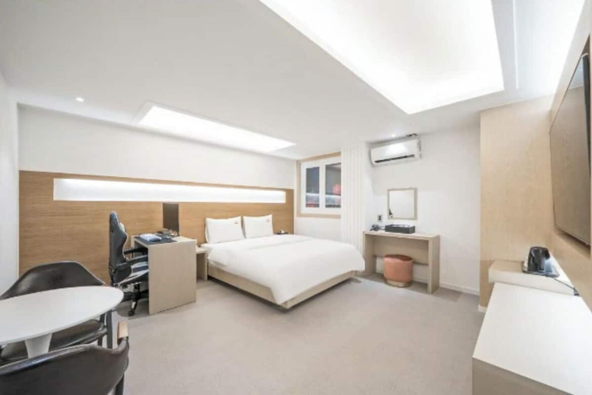 A modern hotel room with a bed, desk, chair, and a large window.