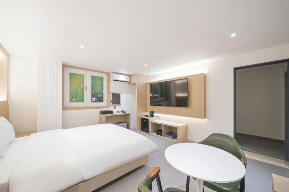 Een hotelkamer met een bed, een ronde tafel, een stoel, een televisie en kunstwerken aan de muren.