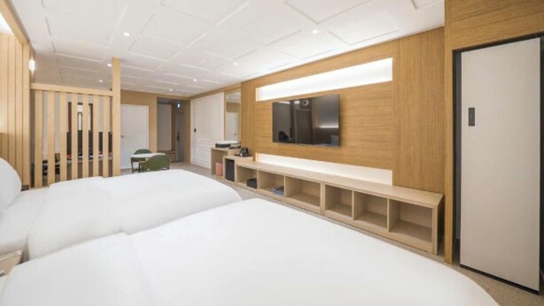 A modern hotel room with two beds, a wooden bench, a TV, and a door. - DEUMEU HOTEL (Changwon)