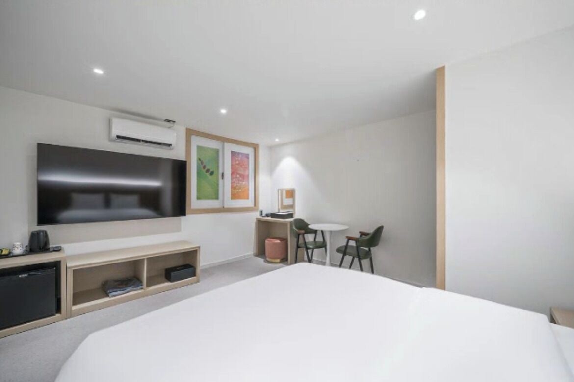 Een moderne hotelkamer met een groot bed, een flatscreen televisie, een bureau met lamp en een klein zithoekje.
