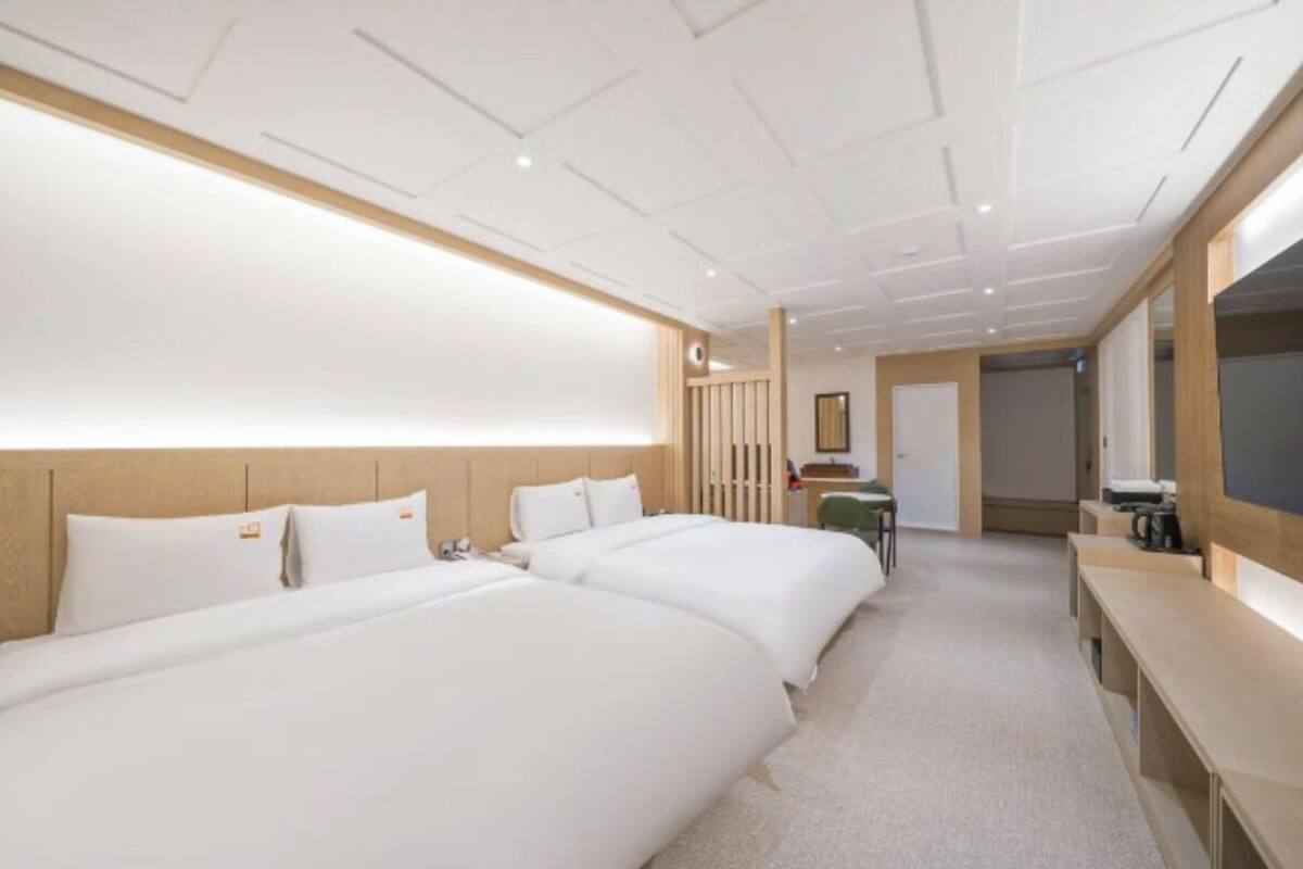 A hotel room with two beds, a desk, a chair, and a large mirror.