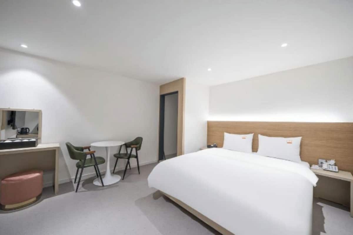 A hotel room with a bed, bedside table, chair, desk, and a small round table.