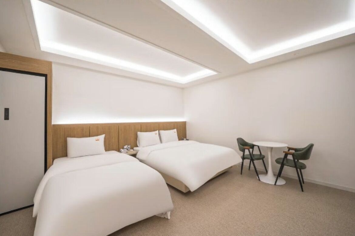 A hotel room with two beds, a small table with chairs, and a skylight.