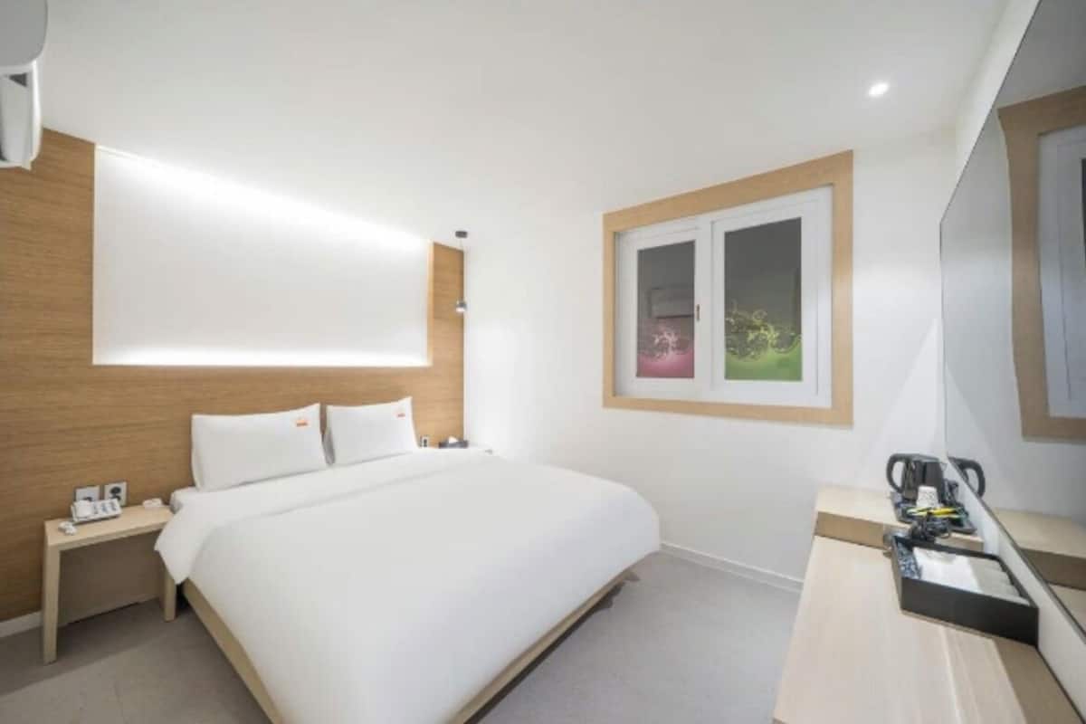 A hotel room with a bed, bedside table, and a small desk with a chair.
