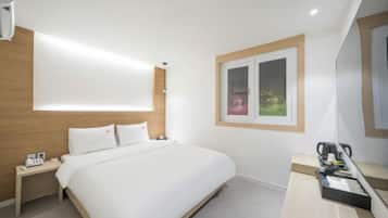 A hotel room with a bed, bedside table, and a small desk with a chair.
