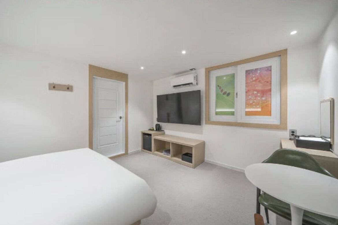 Un dormitorio con una cama, un escritorio, una silla, un televisor y un estante pequeño.