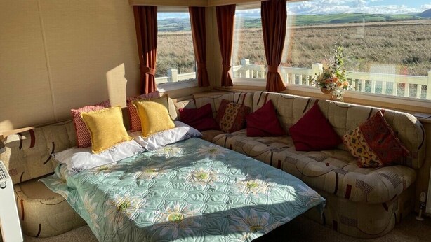 Un dormitorio con cama, sofá, ventana con cortinas y un reloj en la pared.