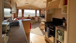 Interior compacto de una caravana con kitchenette, zona de comedor y espacio de estar con vistas.