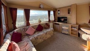 Interior acogedor de una casa rodante con sofá, televisor y zona de comedor.