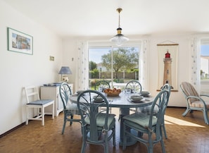 A dining area with a round table, chairs, and a view of a lighthouse. - Holiday for 8 with pool, sea ​​300 m away (Barbâtre)
