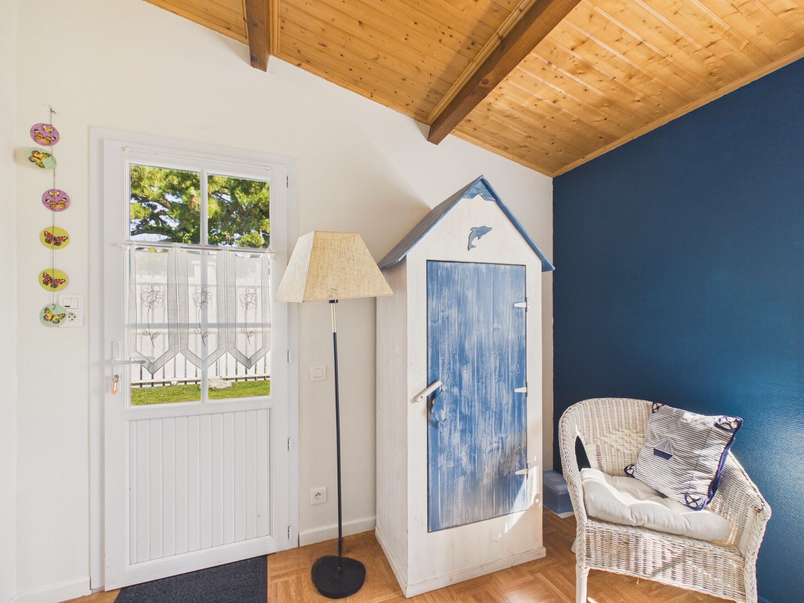 Ein Zimmer mit einer weißen Tür, einer blauen Tür, einem Korbstuhl und einer Stehlampe.