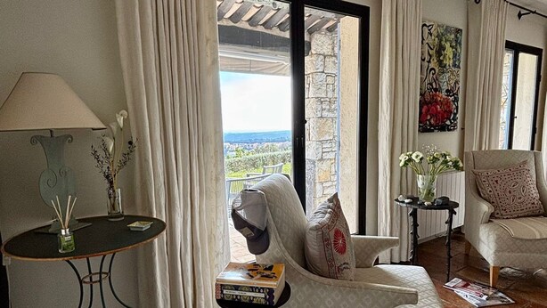 A living room with a sofa, a table with books, a lamp, and a view through a glass door. - Villa BOUGAINVILLEA, magnificent villa on the heights of Vence. (Vence)