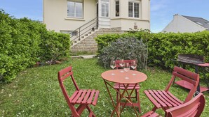 Ein Haus mit einer Steintreppe, die zu einer Tür führt, einer kleinen Terrasse mit Tisch und Stühlen sowie einem gepflegten Garten.
