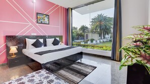 A modern bedroom with a bed, a nightstand, a ceiling fan, a large window, and a view of greenery outside. - Alaya Stays Tranquil Meadows 5BHK Farm (Taoru)