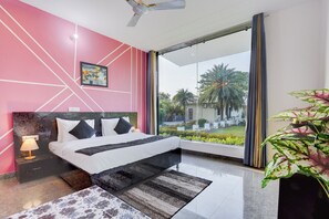 Ein modernes Schlafzimmer mit Bett, Nachttisch, Deckenventilator, einem großen Fenster und Blick auf Grünfläche.