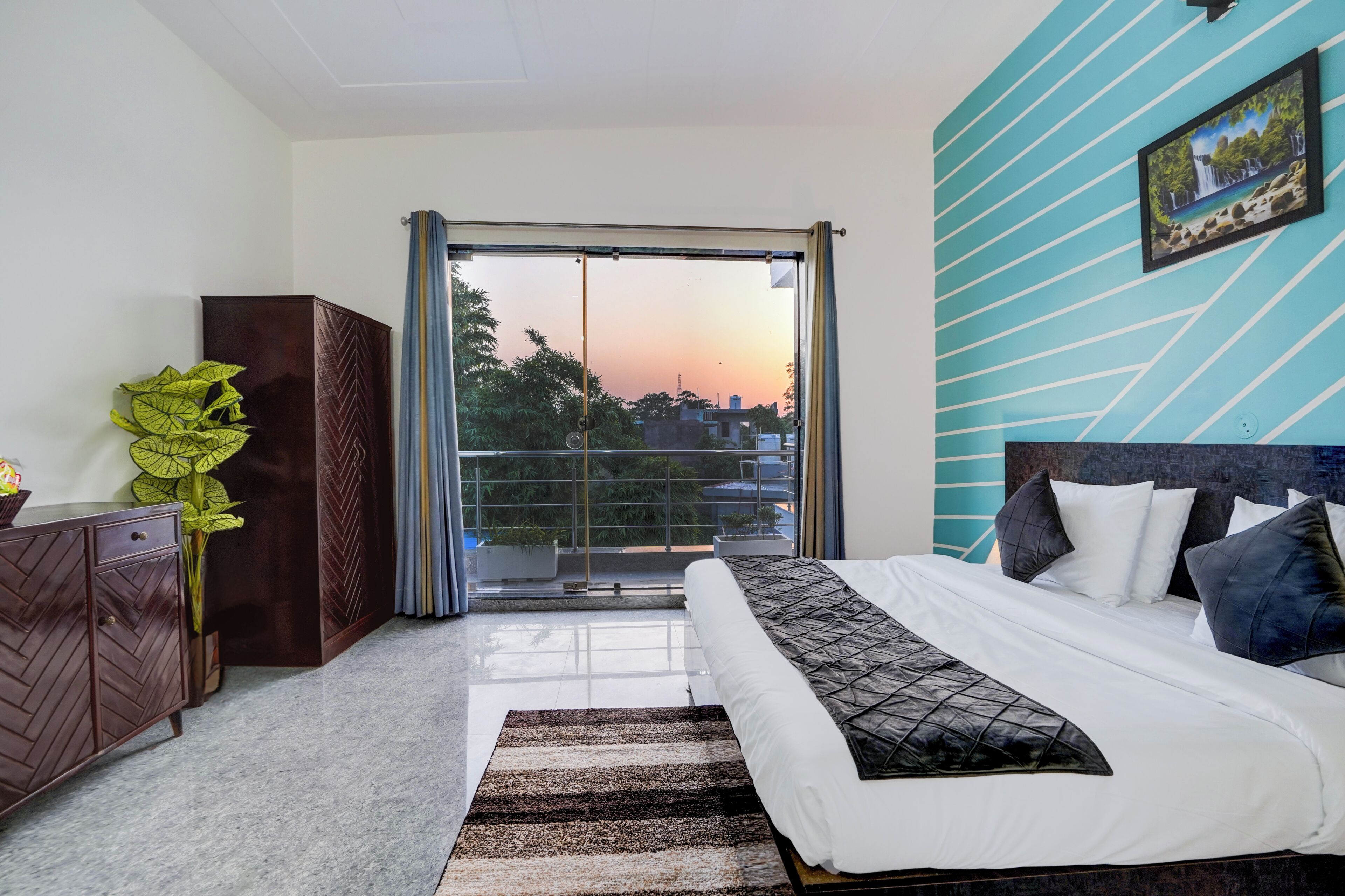 A bedroom with a bed, a view of the sky, a potted plant, and a wardrobe.
