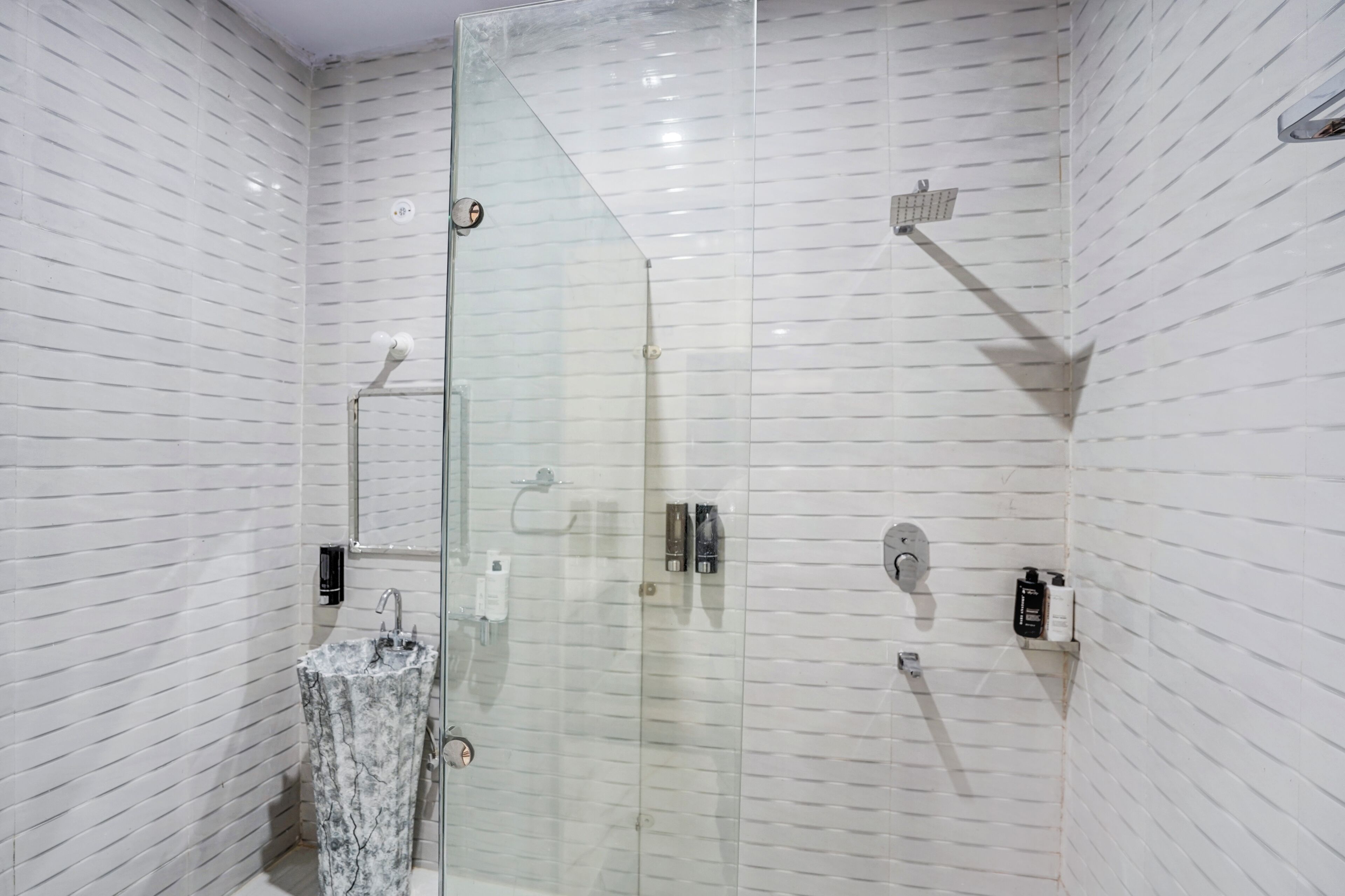 A modern bathroom with a glass-enclosed shower, a marble sink, and a tiled wall.