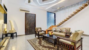 A modern living room with a sofa, coffee table, and chairs, a staircase, and a large window. - Alaya Stays Tranquil Meadows 5BHK Farm (Taoru)
