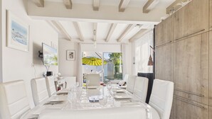A dining area with a table set for four, white chairs, a wooden ceiling, and a view through the glass door. - Family home: beach walk, garden & BBQ (Le Pouliguen)
