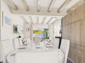 A dining area with a table set for four, white chairs, a wooden ceiling, and a view through the glass door. - Family home: beach walk, garden & BBQ (Le Pouliguen)
