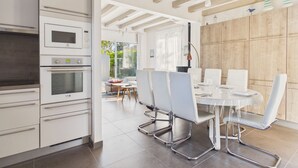 A modern kitchen with built-in appliances, a dining area with a round table and chairs, and a view of the outdoors. - Family home: beach walk, garden & BBQ (Le Pouliguen)