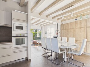 A modern kitchen with built-in appliances, a dining area with a round table and chairs, and a view of the outdoors. - Family home: beach walk, garden & BBQ (Le Pouliguen)