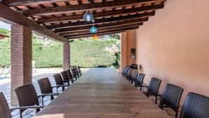 A long wooden table with chairs, a pergola with hanging lights, and a view of greenery. - Residencia occitania-building complex with 5 apartments (Calonge)