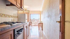 A kitchen with a stove, oven, and cabinets, leading to a dining area with a table and chairs. - Residencia occitania-building complex with 5 apartments (Calonge)