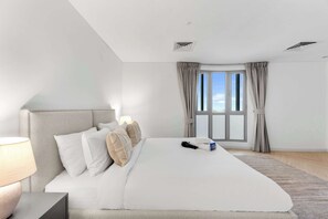 Ein modernes Hotelzimmer mit einem großen Bett, einem Nachttisch, einer Lampe, einer Fernbedienung und einem Fenster mit Vorhängen.