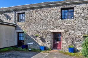 A stone building with a red door, a small window, and potted plants. - Trimstone Manor - Paddock Cottage (Woolacombe)