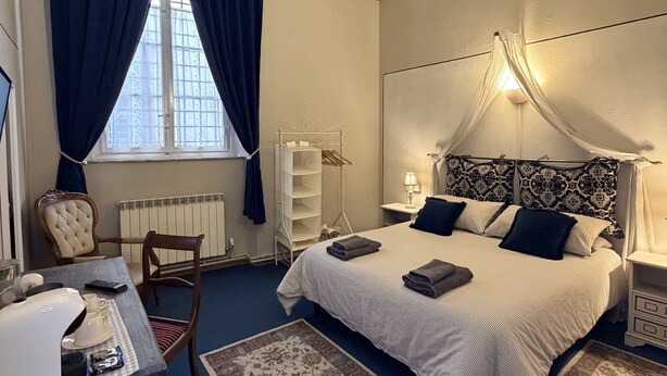 A bedroom with a bed, a desk, a chair, a radiator, and a window with curtains. - Guest Housa Santa Giustina (Lucca)