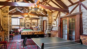 A billiards table, a pool table, and a dartboard in a room with stone walls and wooden beams. - Trimstone Manor - Granary Cottage (Woolacombe)