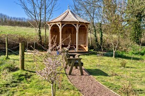 A wooden gazebo with a tiled roof, surrounded by a gravel path and a picnic table. - Trimstone Manor - Mill Apartment (Woolacombe)