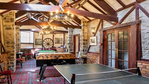 Ein Billardtisch, ein Snookertisch und eine Dartscheibe in einem Raum mit Steinwänden und Holzbalken.