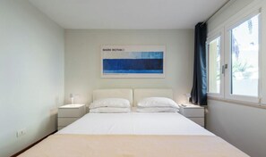 Ein Schlafzimmer mit einem großen Bett, zwei Nachttischen, einem Fenster mit Vorhängen und einem Bild an der Wand.