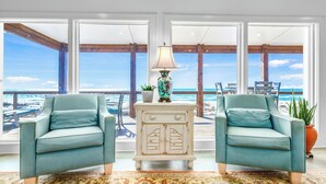A room with two light blue armchairs, a white chest of drawers, a patterned rug, and a view of the ocean through large windows. - Getaway Beach Front, St. George Island Private 4  Bedroom Home (St. George Island)